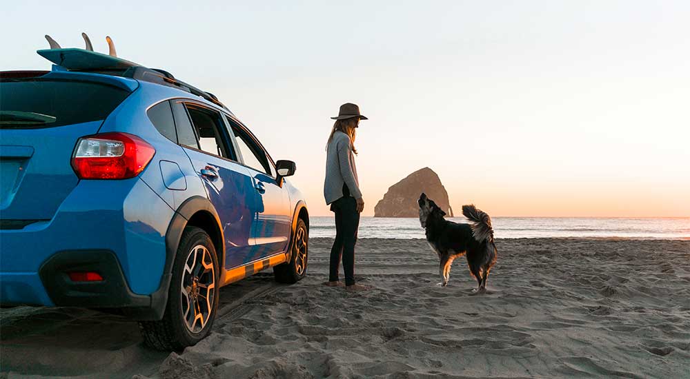 Woman and her dog next to her car at the beach